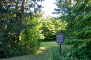An information plaque on Edmund John Zavitz stands at the entrance to a meadow surrounded by trees